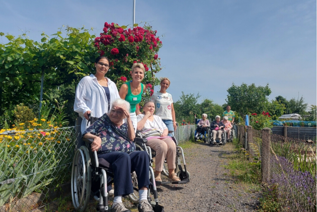 Neuwied: BewohnerInnen und MitarbeiterInnen vor Blumensträuchern zwischen Schrebergärten.