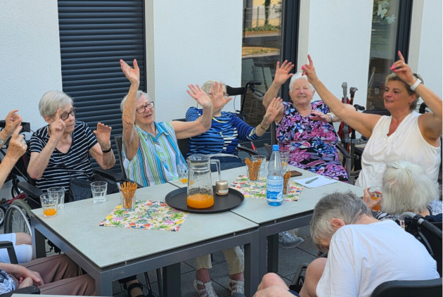 Neuwied: BewohnerInnen und Mitarbeiterin draußen am Tisch halten die Hände nach oben.