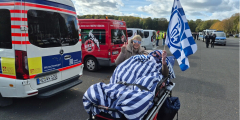 Neuwied: Bewohner mit Schalkeflagge im Bett neben Betreuungsdienstmitarbeiterin auf Stadionparkplatz.